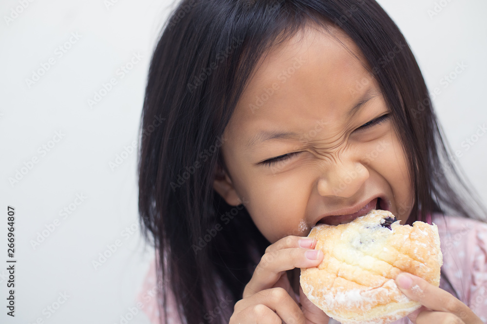 Asian child girl is eating a cream donut. She is enjoying eating unhealthy food Asian child girl is eating a cream donut. She is enjoying eating unhealthy food
