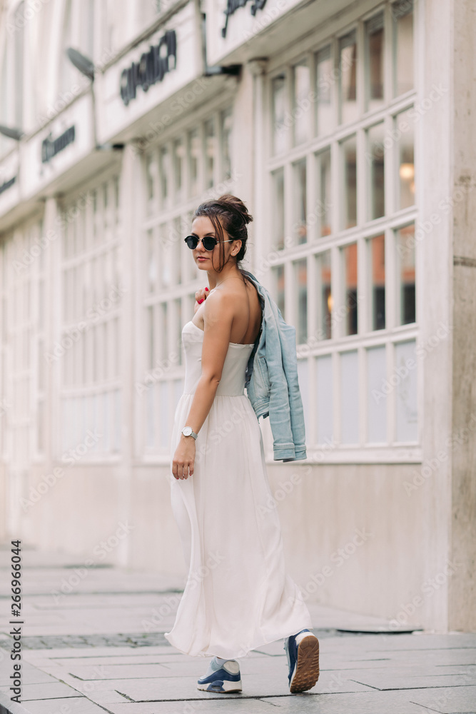 attractive woman in sunglasses and white dress walks through the city streets on a sunny day. girl in the old town attractive woman in sunglasses and white dress walks through the city streets on a sunny day. girl in the old town