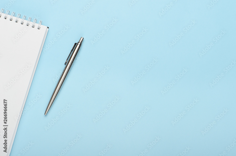 White notepad with metal pen on a blue background. Office, copy space, mock up, template, top view, flat lay. White notepad with metal pen on a blue background. Office, copy space, mock up, template, top view, flat lay.