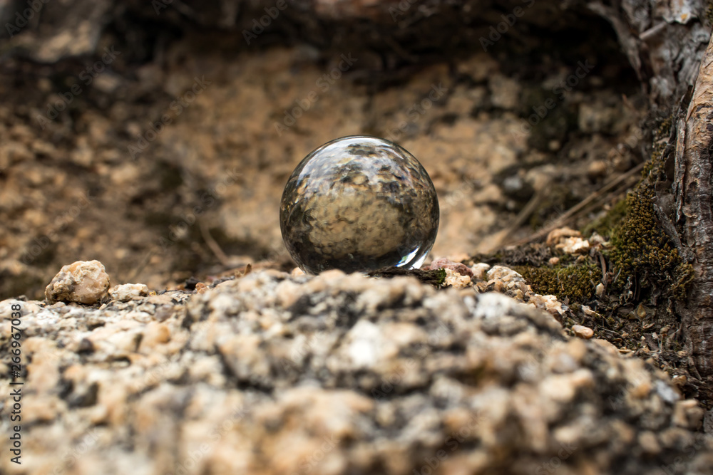 a glass ball lies in the middle on a granite slab next to it grows moss and the roots of the tree are visible a glass ball lies in the middle on a granite slab next to it grows moss and the roots of the tree are visible