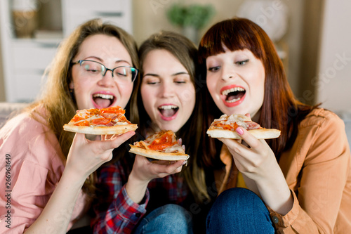 Closeup photo of three cheerful smiling girls celebrating a party at home and eating pizza.