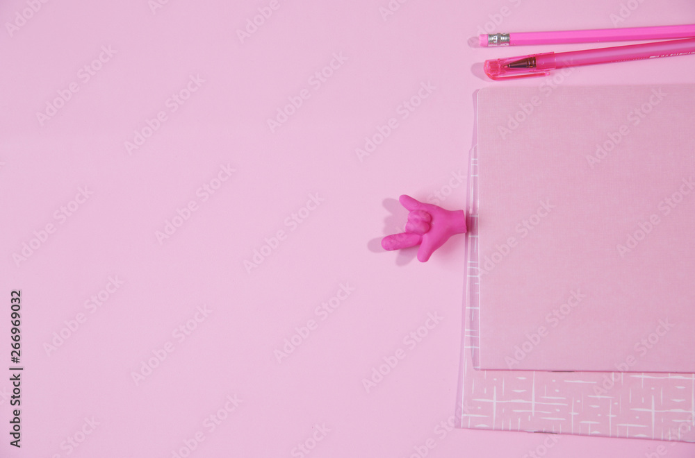 pink notebook and pink pen with a pencil, an eraser in the form of a hand showing a good luck sign on a pink background with copy space for text. Flat lay.
