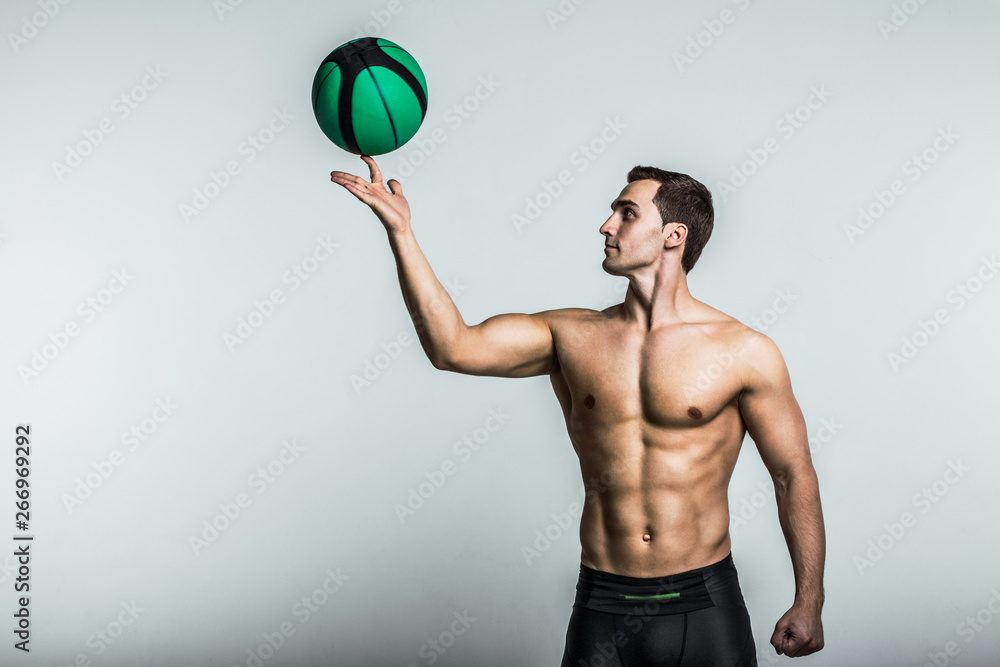 Muscle male model in black treand sportswear posing with a basket ball on gray background. Studio shoot.