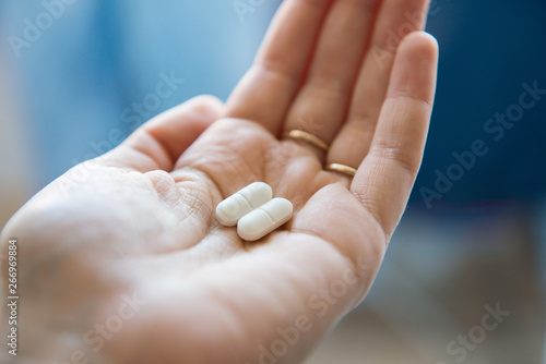 Close-up view of a hand holding two white pills in the palm above a blurry background, painkiller photo