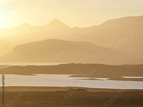 A sunset over the fjord. Sun is setting behind the tall mountains  leaving the scene in golden shades. Calm surface of the water in the fjord. Calm and serene scene. Landscape unspoiled by humans