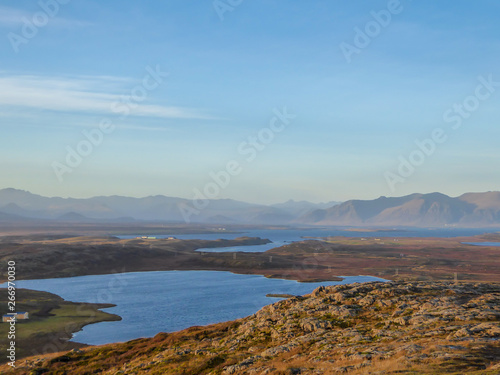A flatland  covered with golden grass. Dried grass due to the winter season. Fjord view  with some taller mountains in the back. Calm water of the fjord. Clear weather with some clouds on the sky.