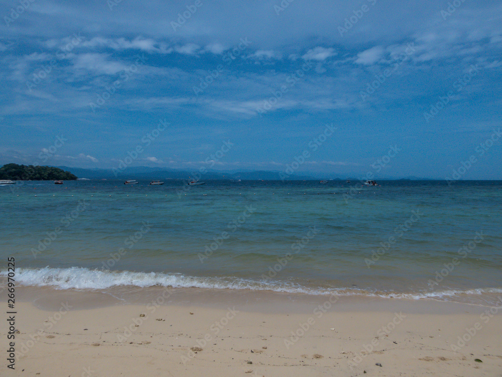 A calm sandy beach on one of the smaller islands in Malaysia. Few boats parked near to the shore. Other islands visible in the back. Clear and nice weather.  Relaxation by the shore.