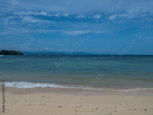A calm sandy beach on one of the smaller islands in Malaysia. Few boats parked near to the shore. Other islands visible in the back. Clear and nice weather.  Relaxation by the shore.