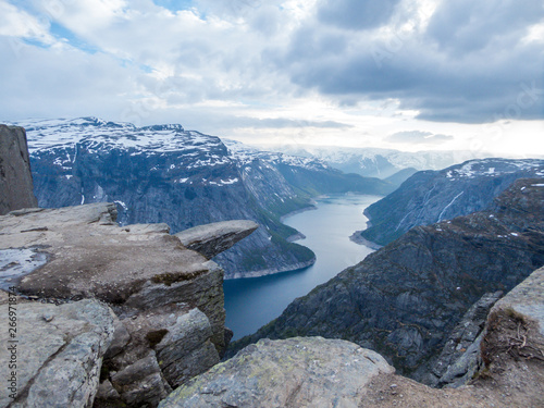 Famous rock formation, Trolltunga with a view from the above on Ringedalsvatnet lake, Norway. Rock hanging. Slopes of the mountains are partially covered with snow. The water of the lake is navy blue. © Chris