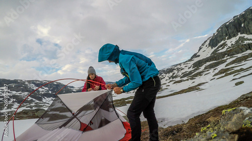 A young couple putting the tent up in the wilderness. The ground is covered with snow. They struggle with the wires. Cold and windy weather. Camping in the unfavorable weather conditions. photo