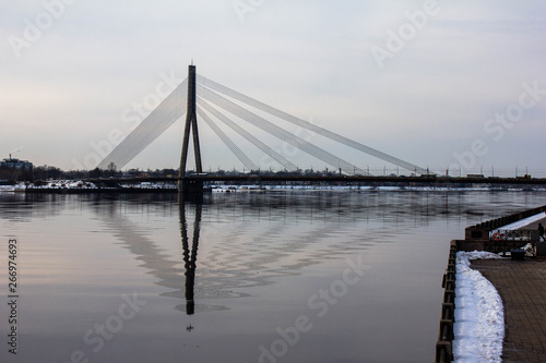 Huge suspension bridge and its refliction in a wide river Daugava during winter period in Riga, Latvia. © Daniil