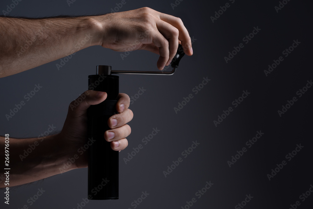 Fototapeta premium A man grinds grain coffee with a manual coffee grinder. Dark background