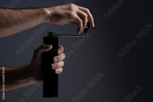 A man grinds grain coffee with a manual coffee grinder. Dark background