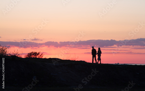 silhouette of man and woman walking on beach at sunset