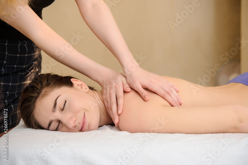 lateral view of a young woman receiving a neck and shoulders massage done by a masseuse in a spa salon