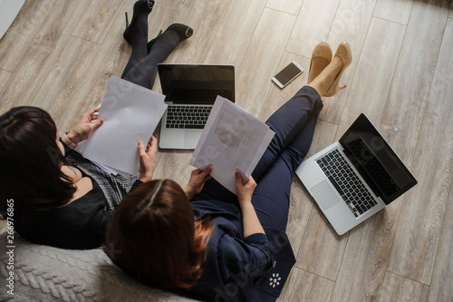 top view of two women in business outfit sitiing on the floor working on computers and discussing a report photo