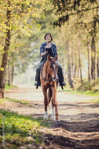 portrait of happy young woman riding horse with cordeo in the morning in spring forest © vprotastchik