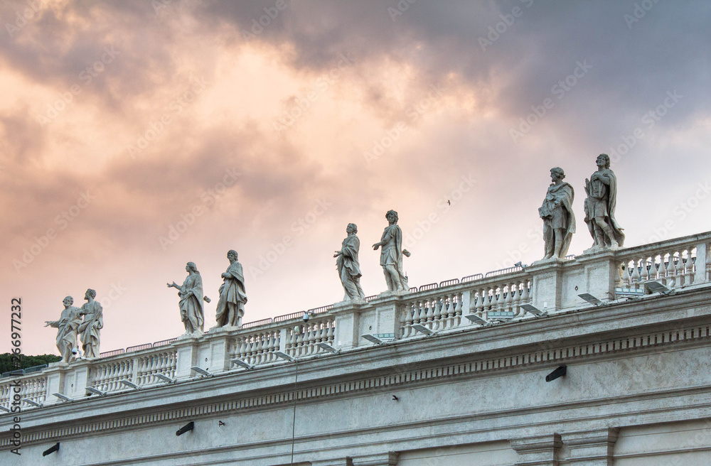Roof of Saint Peter's Cathedral in the Vatican with various statues and sculptures on it, columns below and cathedral's dome above and on the right. Vatican, Rome, Italy