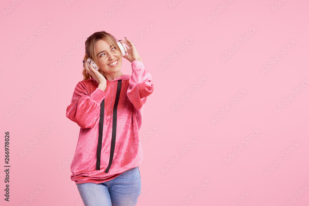 Fototapeta premium Wireless connection. Portrait of young woman posing isolated over pink background listening fun music with headphones.