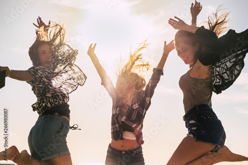 Youthful people beautiful young girl jumping and celebrating for happiness outdoor with sun in backlight - have lot of fun and laugh together in friendship - happy lifestyle concept