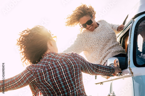 Freedom and travel people lifestyle concept - blonde beautiful curly middle age young woman out of the window of old vintage van enjoying the sunny day with friend outside having fun together photo