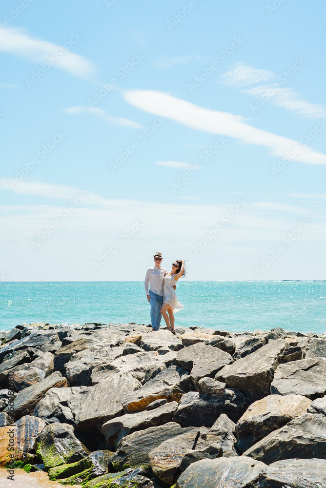 A young couple of lovers, a guy and a girl on the ocean, in white clothes on the stones.