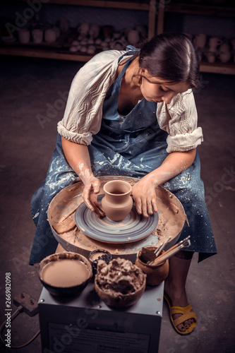 Stylish handicraftsman master making pottery, sculptor from wet clay on wheel. Artisan production.