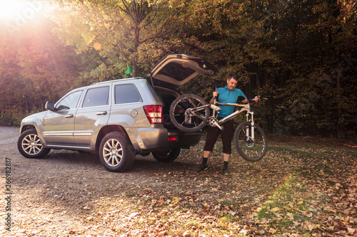 Man on forest car park unloading mountain bike from car