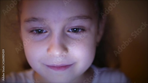 Night Shot of a Cute Caucasian Little Girl Close Up of a Child's Face Viewing a Tablet PC With a Reflection of Pight and Pictures in His Eyes photo