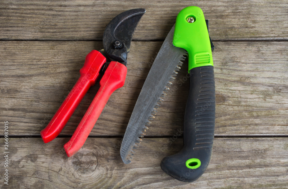 Gardeners hand tools - folding saw and pruner. Garden tools are on a wooden table. Gardeners hand tools - folding saw and pruner. Garden tools are on a wooden table.