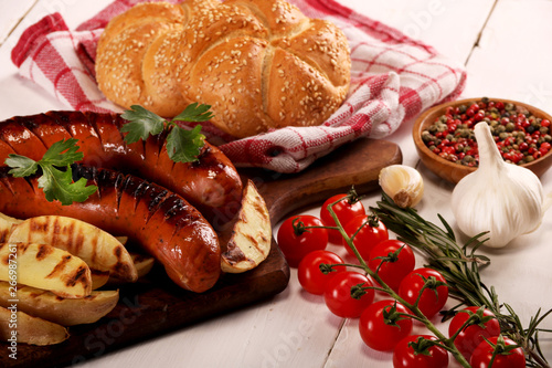 Grilled sausages with vegetables, spices and bread on wooden cutting board background