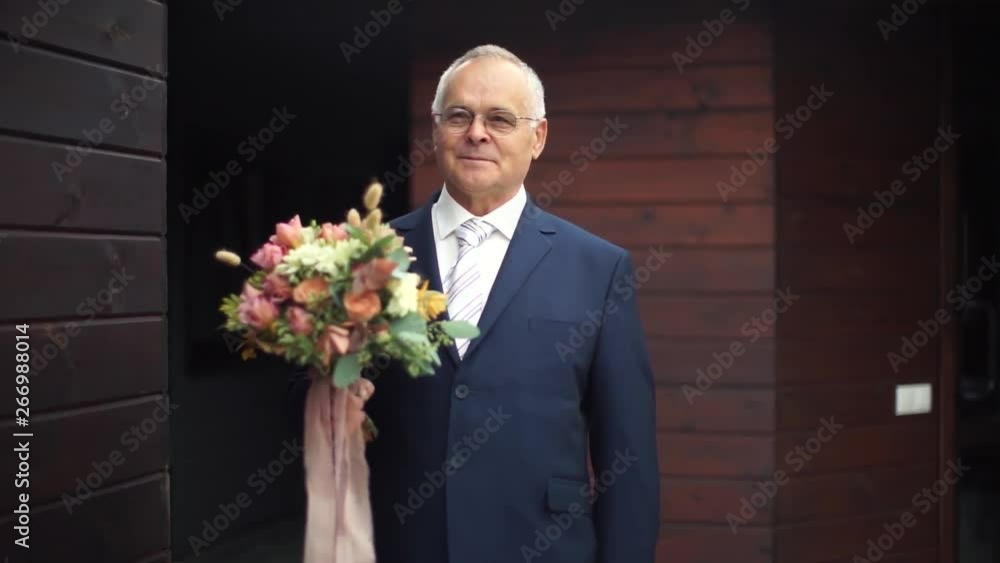 An elderly man holding a bouquet of roses. Old man suit holding flowers. The old man smiles at the camera. An elderly man holding a bouquet of roses. Old man suit holding flowers. The old man smiles at the camera.