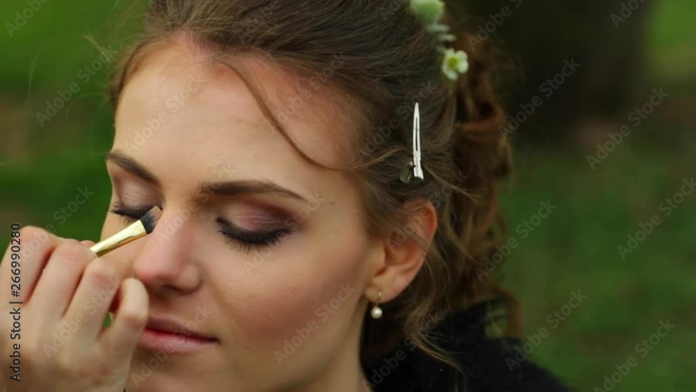 Applying make up around eyes to bride before stylist wedding during sunny day on bench Applying make up around eyes to bride before stylist wedding during sunny day on bench