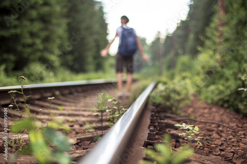 Railway track passes through the forest, on a blurred background stands a confused tourist with a backpack, which is lagging behind the train.
