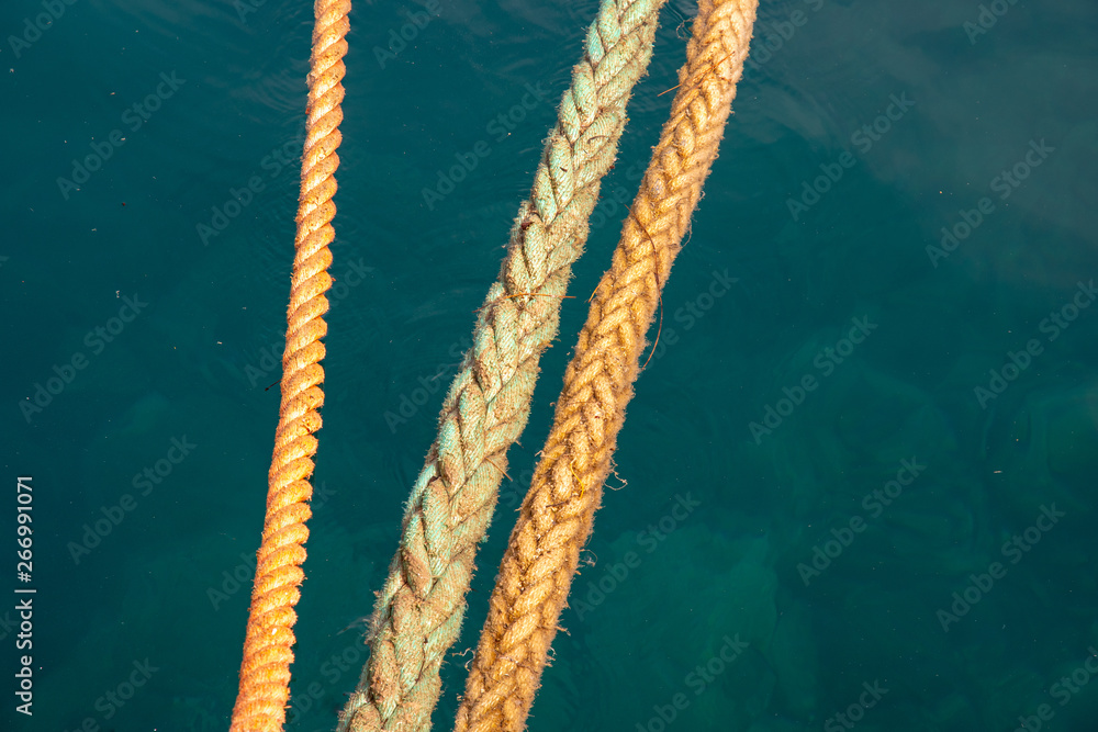 Close-up of three orange braided nautical ropes taut on the sea water in a port, Sestri Levante, Liguria, Italy
