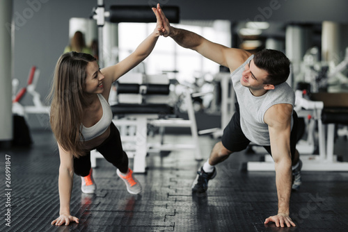 Happy sporty couple giving high five to each other while doing push up together in gym. Unity and support, copy space