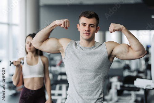 Beautiful sports couple is showing their muscles while standing in gym