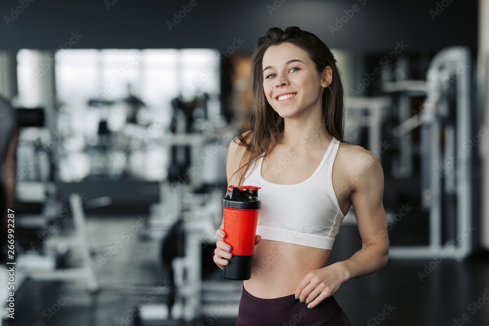 Smiling sporty woman holding bottle of water in gym. Smiling sporty woman holding bottle of water in gym.