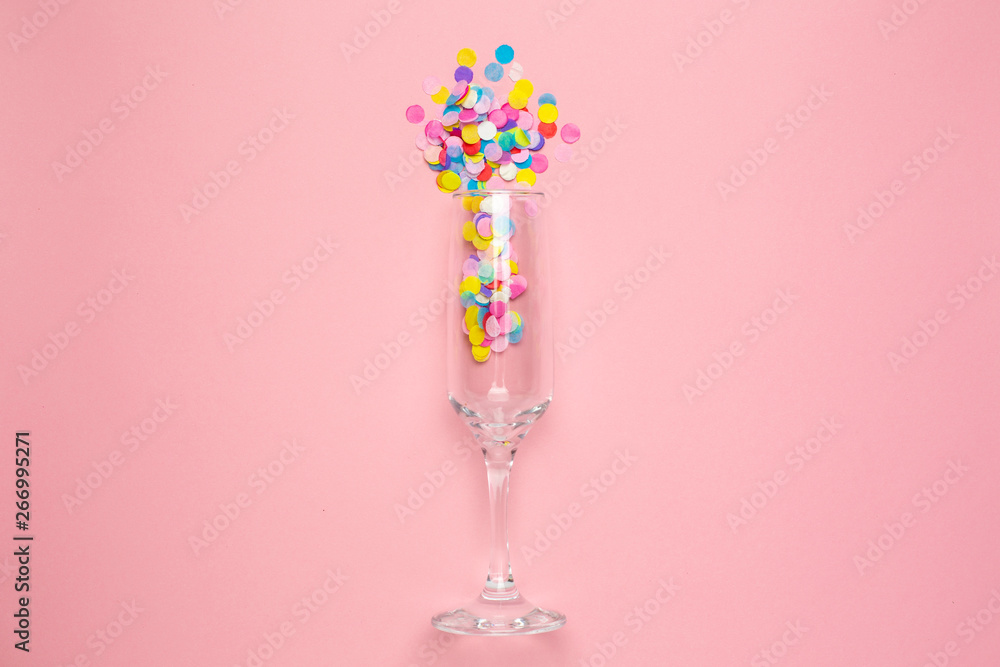 Champagne glass with multi-colored confetti on pink color paper background . Flat lay composition for birthday, mother day or wedding Champagne glass with multi-colored confetti on pink color paper background . Flat lay composition for birthday, mother day or wedding