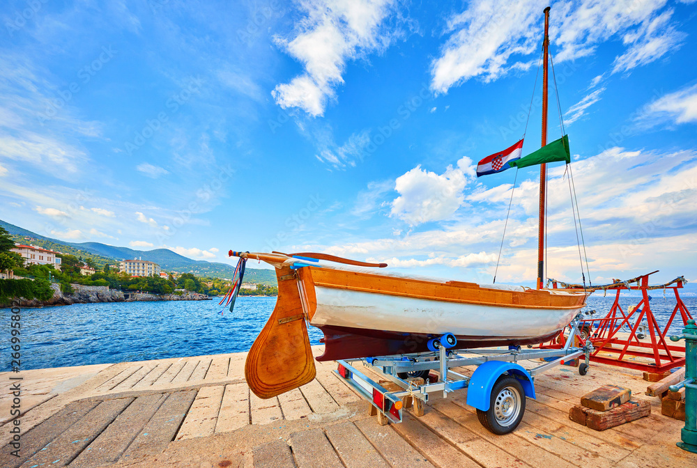 Lovran, Croatia. Sailing wooden boat at piers by sea. Boat trailer for yacht transportation. Sunny summer day and blue sky with clouds.