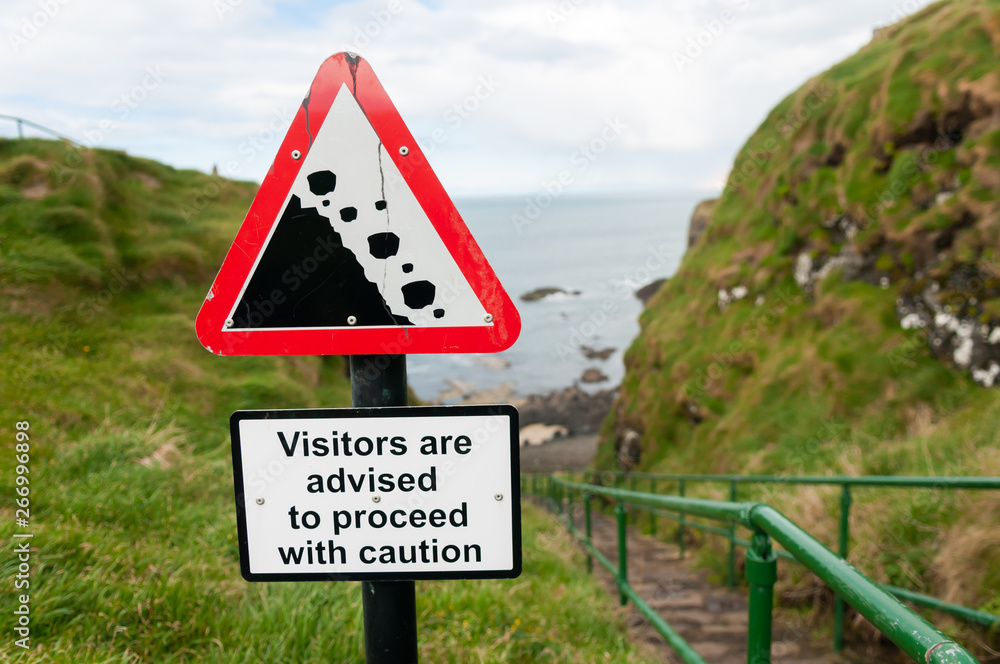 Falling rocks sign on a path beside a seaside cliff warning 
