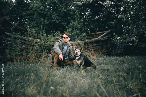young male traveler in a green jacket, in sunglasses with a dog in the forest