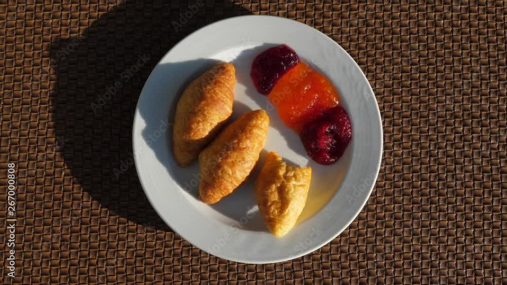 Three small croissants and jam on plate, top hand held view. One bun have bite off, someone eating pastry for breakfast Three small croissants and jam on plate, top hand held view. One bun have bite off, someone eating pastry for breakfast