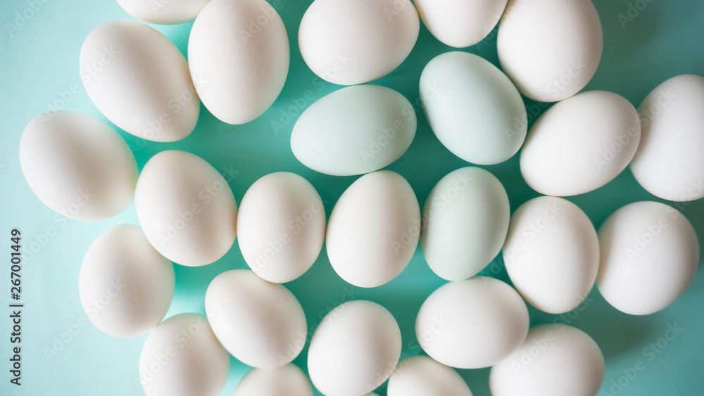Organic white chicken eggs with pale blue accents chaotically lie on a blue background texture top view