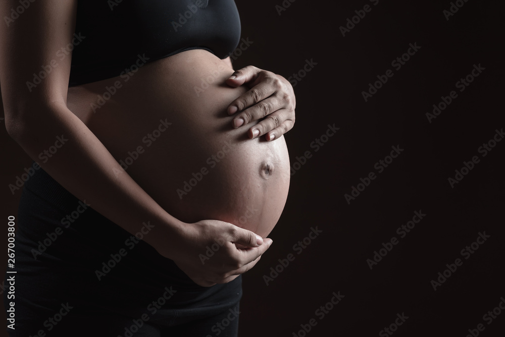 Pregnant woman hands on belly with black background Pregnant woman hands on belly with black background