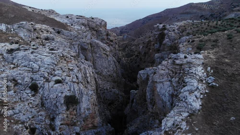 Scenic aerial shot of beautiful canyon, camera fly over rough rocky cliffs at mountainous landscape of Southern Crete. Beautiful view of Portela gorge from air at evening twilight Scenic aerial shot of beautiful canyon, camera fly over rough rocky cliffs at mountainous landscape of Southern Crete. Beautiful view of Portela gorge from air at evening twilight
