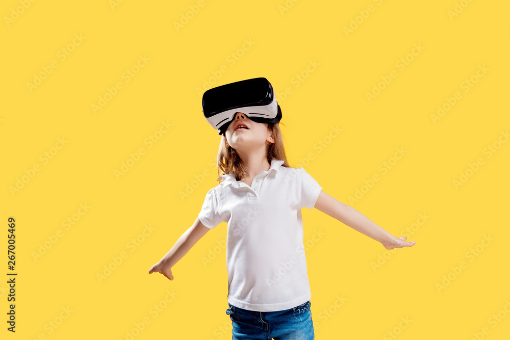 Girl 7 y.o in formal outfit wearing VR glasses putting hands out in excitement isolated on yellow background. Child using a gaming gadget for virtual reality. Virtual technology. Girl 7 y.o in formal outfit wearing VR glasses putting hands out in excitement isolated on yellow background. Child using a gaming gadget for virtual reality. Virtual technology.