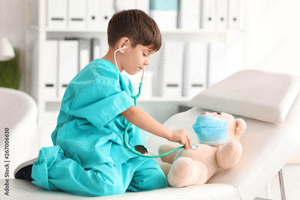 Cute little boy in doctor uniform playing with toy bear in hospital Cute little boy in doctor uniform playing with toy bear in hospital