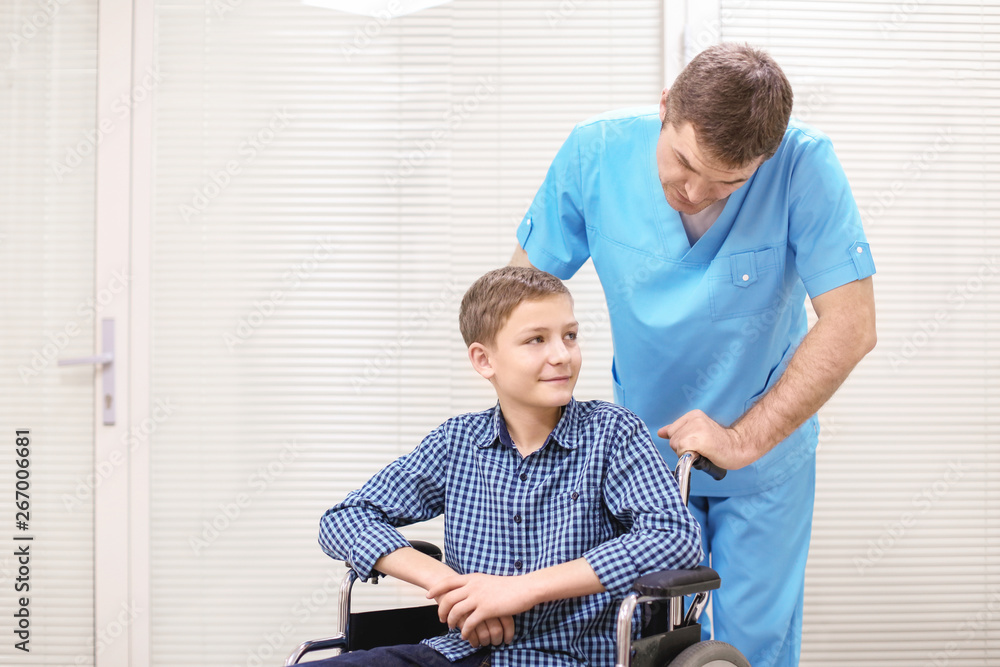 Fototapeta premium Male doctor taking care of little boy in wheelchair indoors