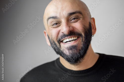Close-up portrait of bearded bald man with earring and beautiful white teeth